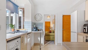 A compact kitchen with a washing machine, a coffee machine, and a clock on the wall. - Heathcoat Apartment with Courtyard (Leicestershire)