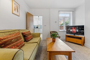 A living room with a sofa, a coffee table, a television, and a potted plant.