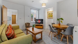 A modern living room with a sofa, coffee table, and a dining area with chairs and a table. - Heathcoat Apartment with Courtyard (Leicestershire)