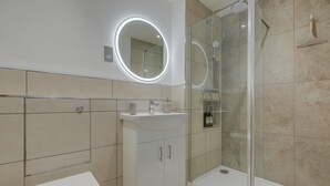 Un baño moderno con inodoro, lavamanos y cabina de ducha con mampara de vidrio.