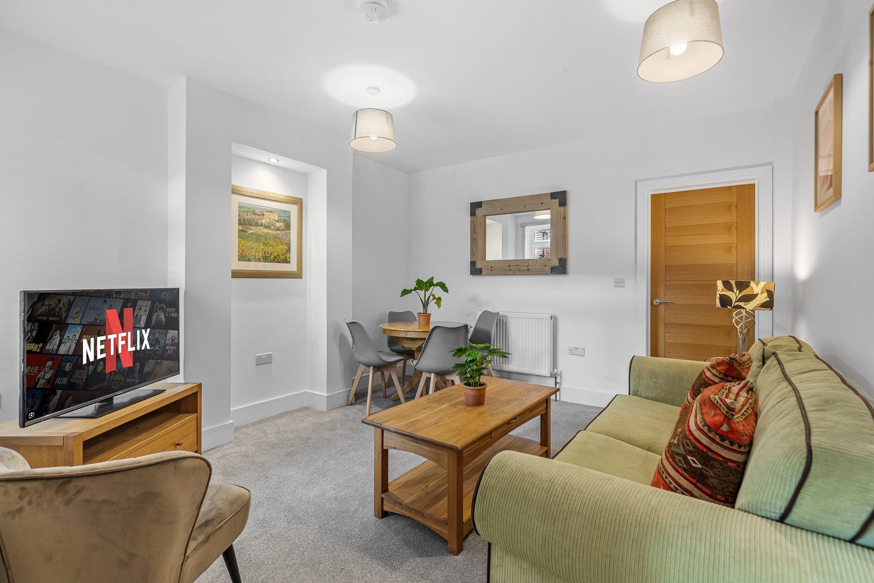 A modern living room with a flat-screen TV, a wooden coffee table, a sofa, and a dining area with chairs and a table.