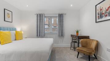 A bedroom with a bed, a desk, a chair, and a window with curtains.
