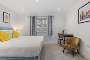 A bedroom with a bed, a desk, a chair, and a window with curtains.