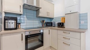 A modern kitchen with white cabinets, a built-in oven, a microwave, a toaster, and a coffee machine. - Heathcoat Apartment with Courtyard (Leicestershire)