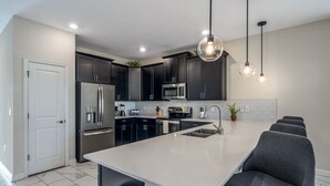 A modern kitchen with dark cabinets, stainless steel appliances, a large island with seating, and pendant lighting. - Champions Gate 8BR Villa-Pool, Game Room, Theater (Four Corners)