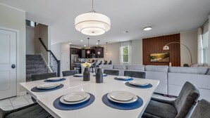 A modern dining area with a white table, dark chairs, and blue placemats. - Champions Gate 8BR Villa-Pool, Game Room, Theater (Four Corners)