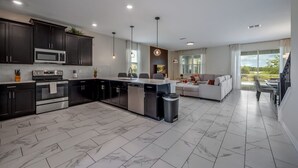A modern kitchen with dark cabinets, stainless steel appliances, and a marble floor. - Champions Gate 8BR Villa-Pool, Game Room, Theater (Four Corners)
