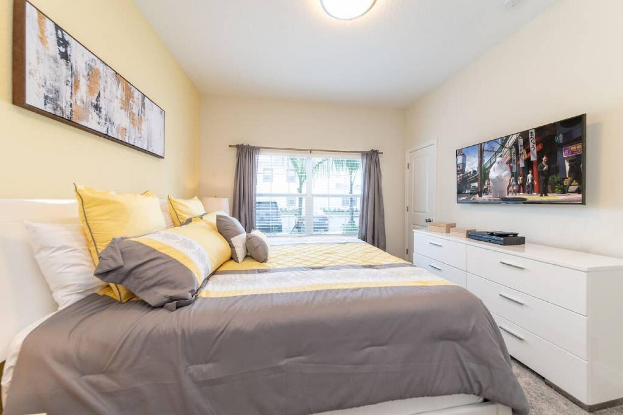 Une chambre à coucher avec un lit, une commode, un tableau et une fenêtre avec des rideaux.