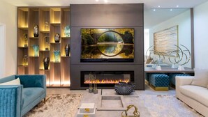 Een moderne woonkamer met een grote flatscreen televisie boven een haard, omringd door planken met decoratieve objecten en een blauwe bank.