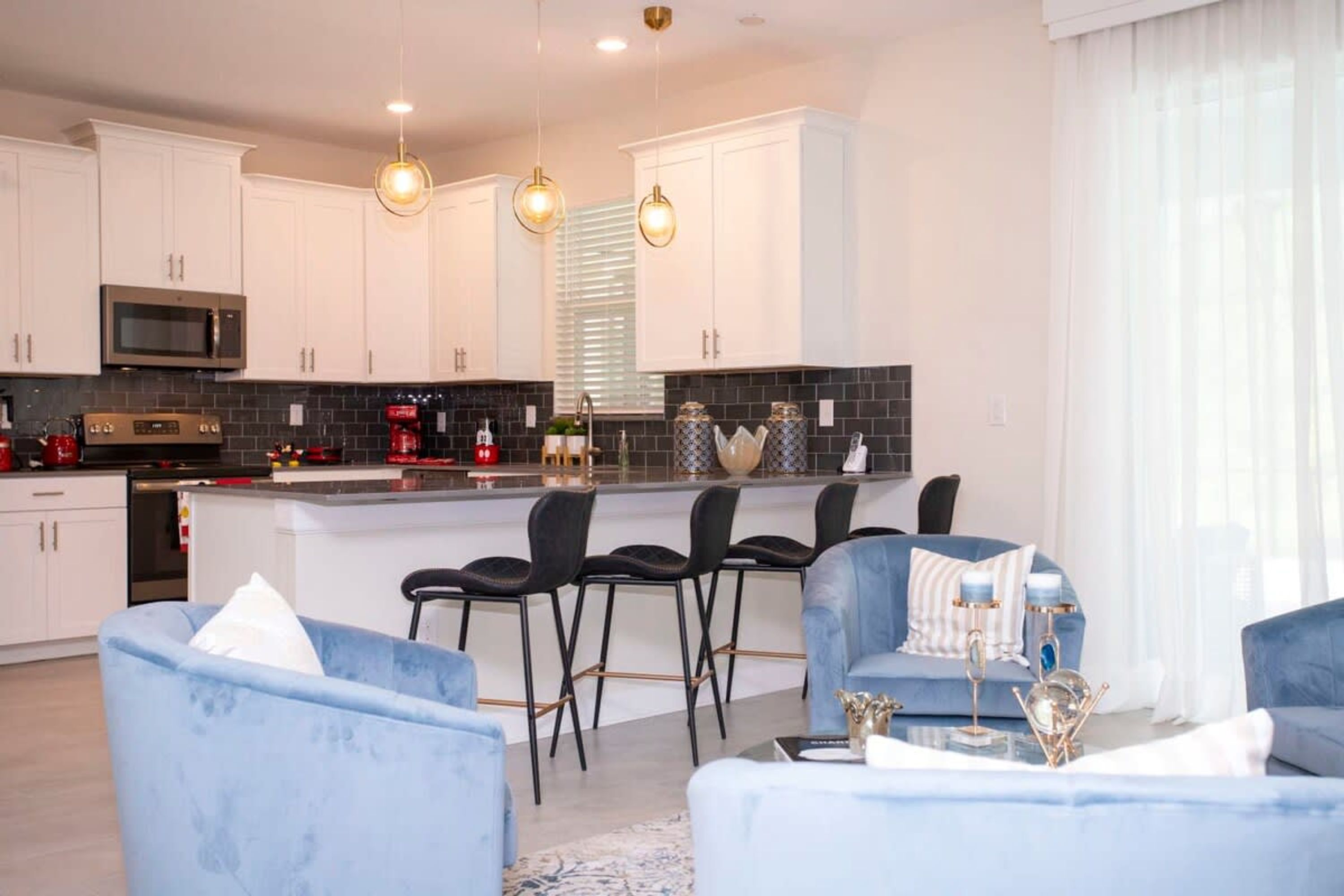 A modern kitchen with white cabinets, a central island with bar stools, and pendant lighting.