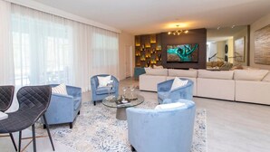 Een moderne woonkamer met een grote bank, twee fauteuils, een salontafel en een tv-wand kunstwerk.