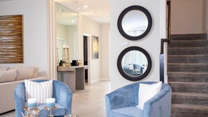 Een moderne woonkamer met twee blauwe fauteuils, een salontafel met decoratieve objecten, en een trap met een leuning.