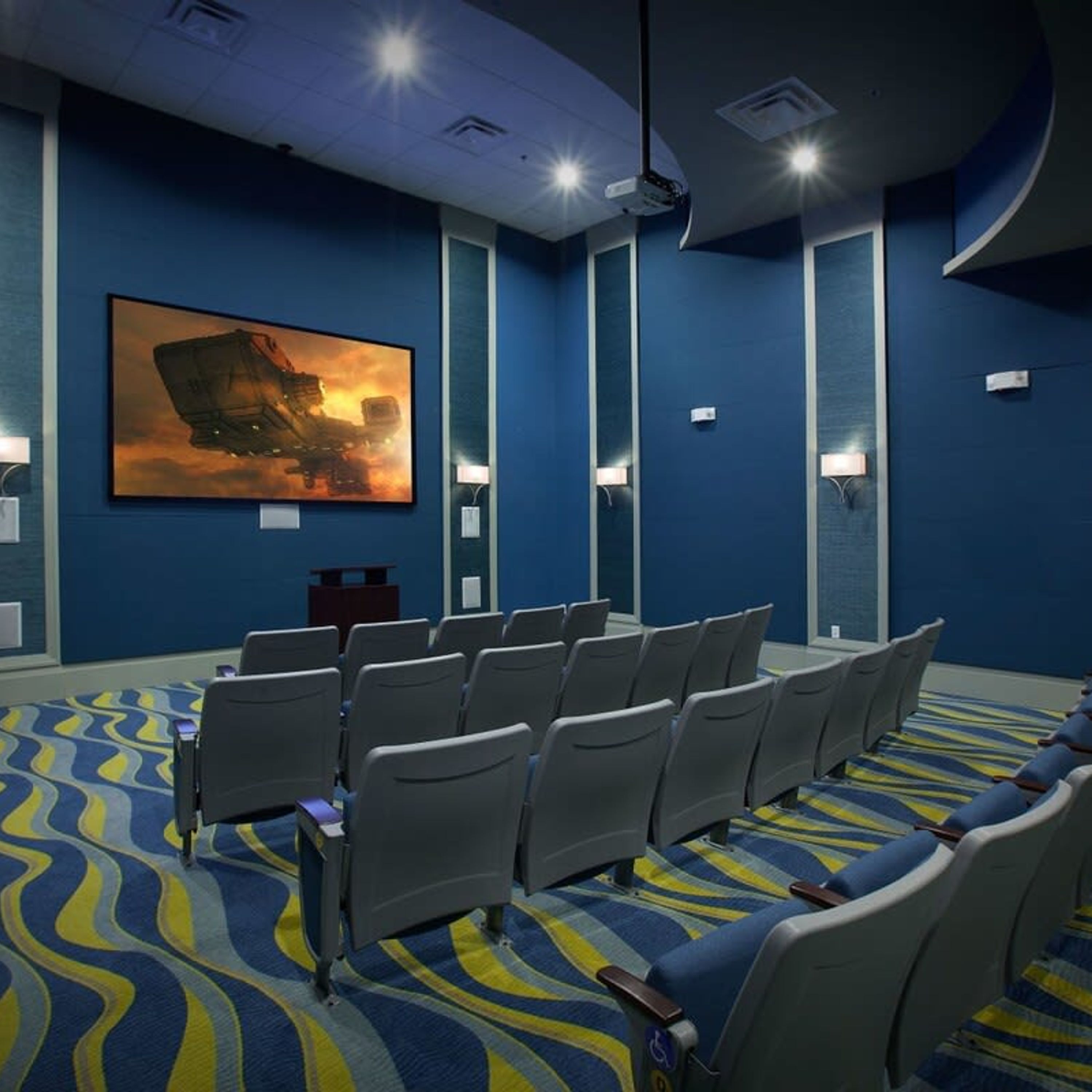 A conference room with rows of chairs, a large screen, and a projector.