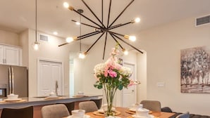 Un comedor moderno con una mesa de madera dispuesta para cuatro personas, rodeada de sillas grises. Un original candelabro negro con múltiples bombillas cuelga encima.