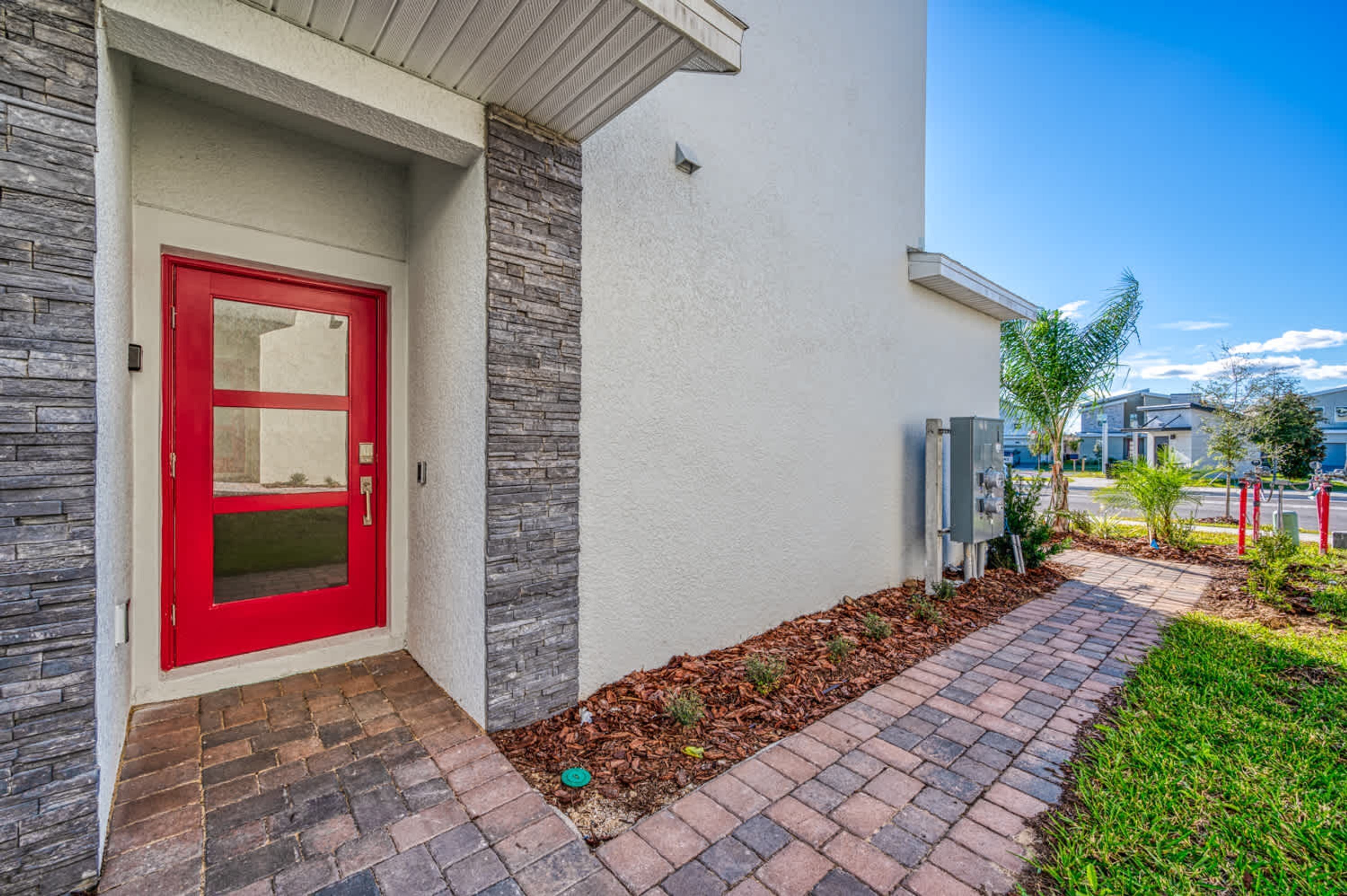 A modern building with a red door, stone accents, and a paved walkway leading to the entrance.