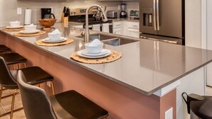 Una cocina moderna con armarios blancos, un refrigerador de acero inoxidable, un microondas y una isla grande con taburetes de bar.