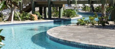 A swimming pool with a curved design, surrounded by palm trees and a fence.