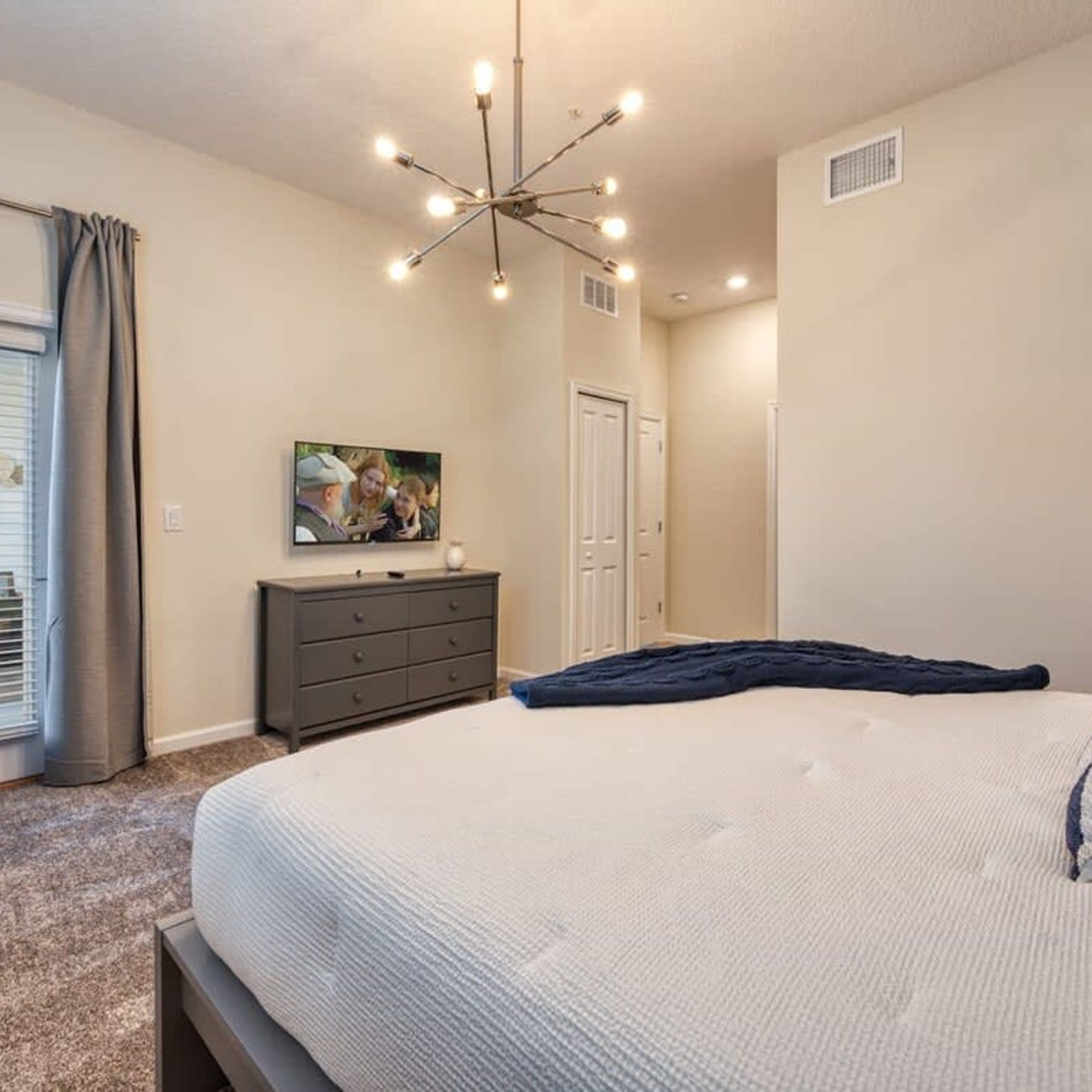Une chambre à coucher avec un grand lit, une commode, un tableau au mur et un luminaire au plafond.