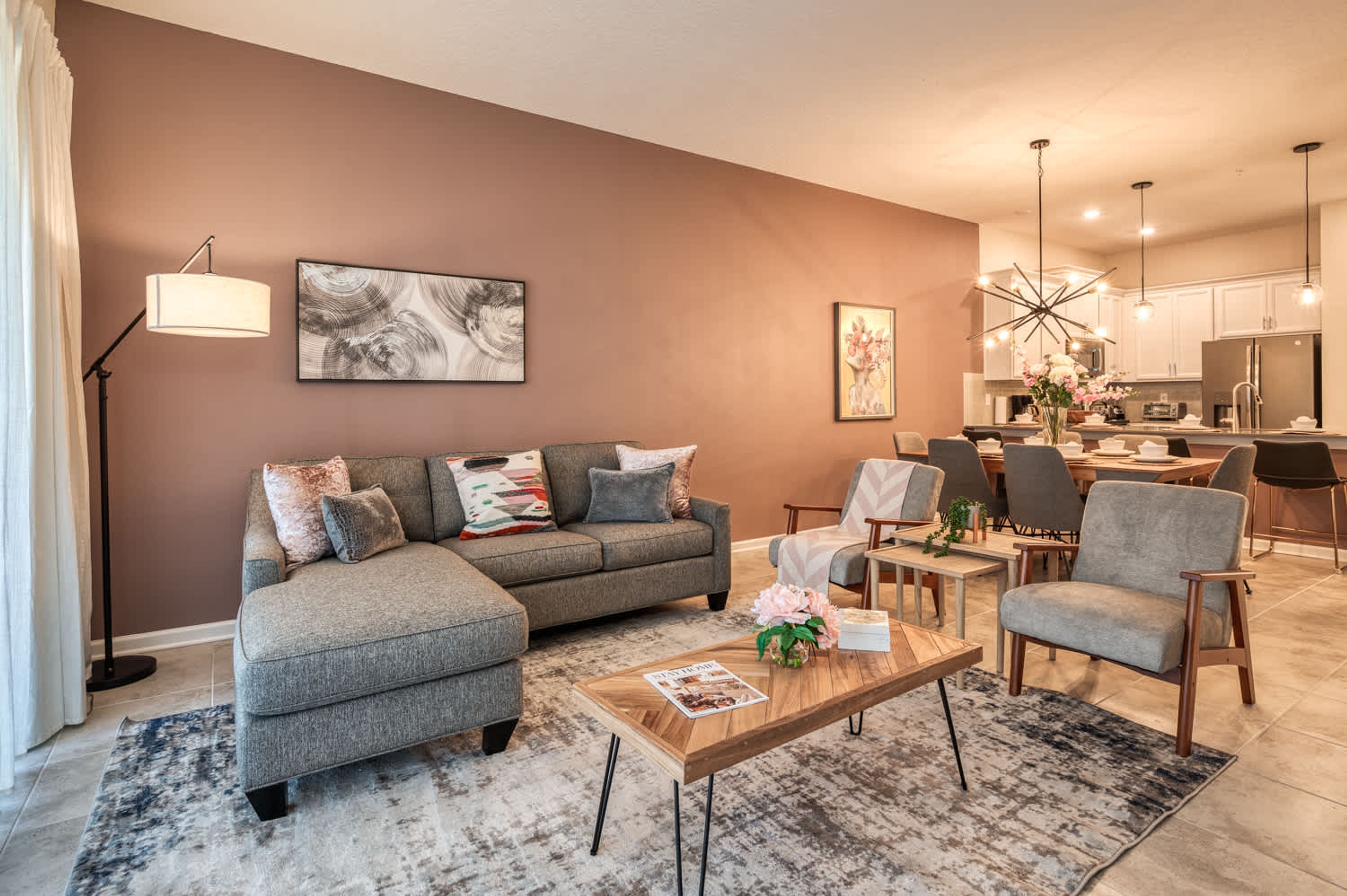 A modern living room with a sectional sofa, a coffee table, and a dining area with chairs and a kitchen in the background.