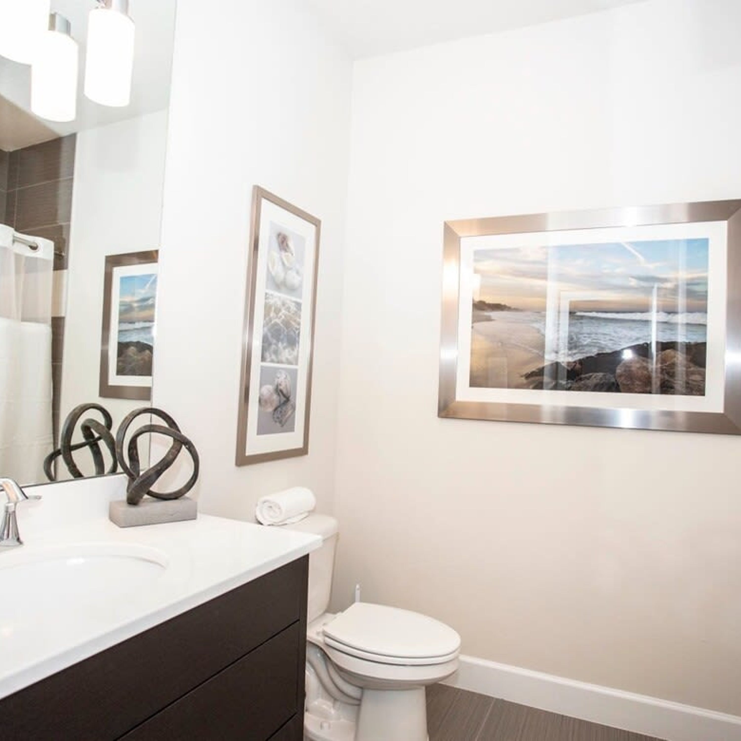 Un bagno moderno con un lavandino bianco, un mobile vanit脿 dai toni scuri, un WC e opere d'arte incorniciate alle pareti.
