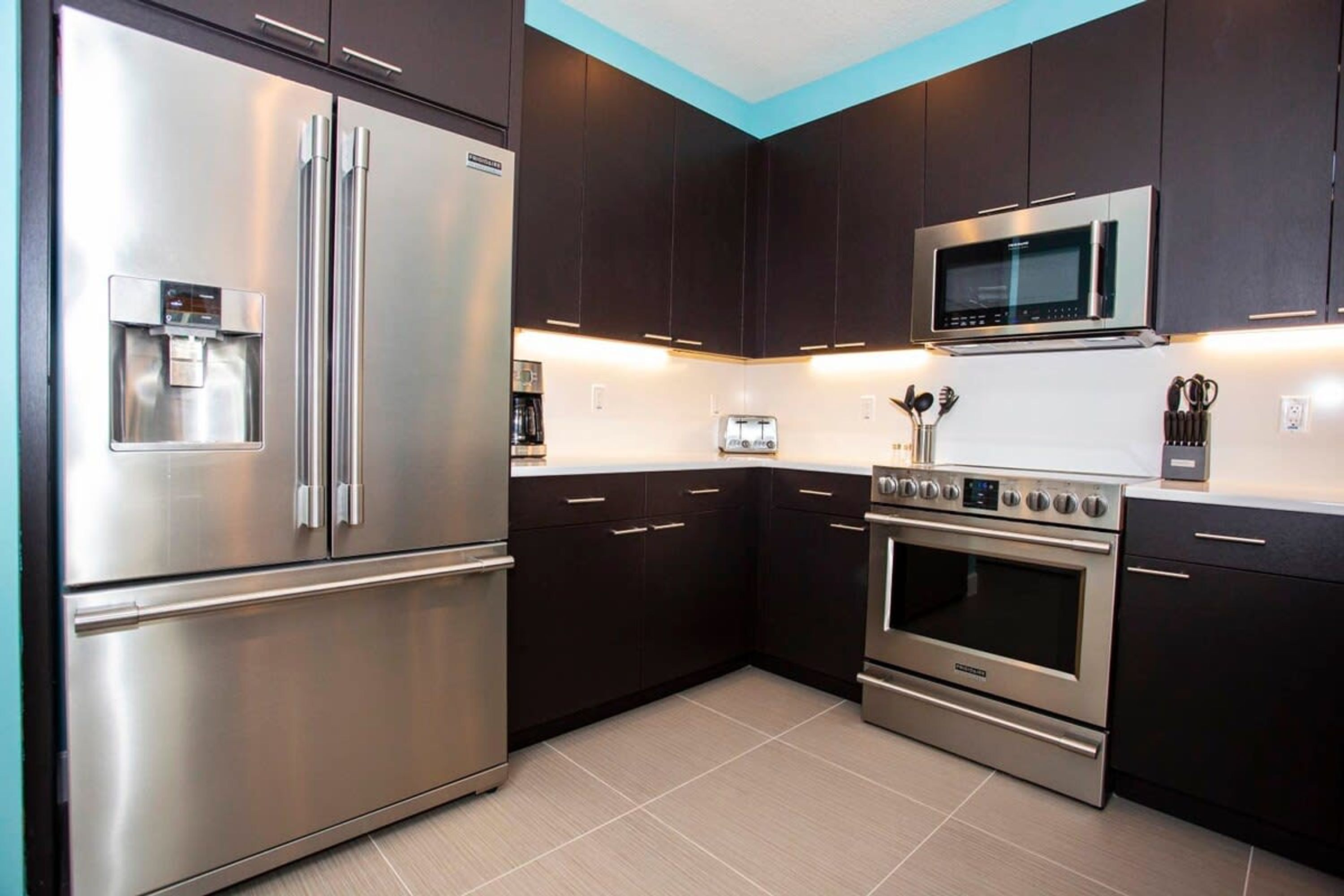 A modern kitchen with stainless steel appliances, dark cabinetry, and a tiled floor.