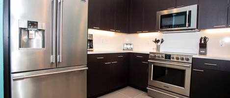 A modern kitchen with stainless steel appliances, dark cabinetry, and a tiled floor.