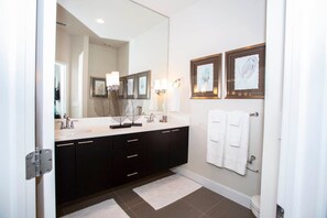 Une salle de bain moderne avec un grand miroir, deux lavabos, des meubles de rangement aux couleurs sombres et des toilettes.