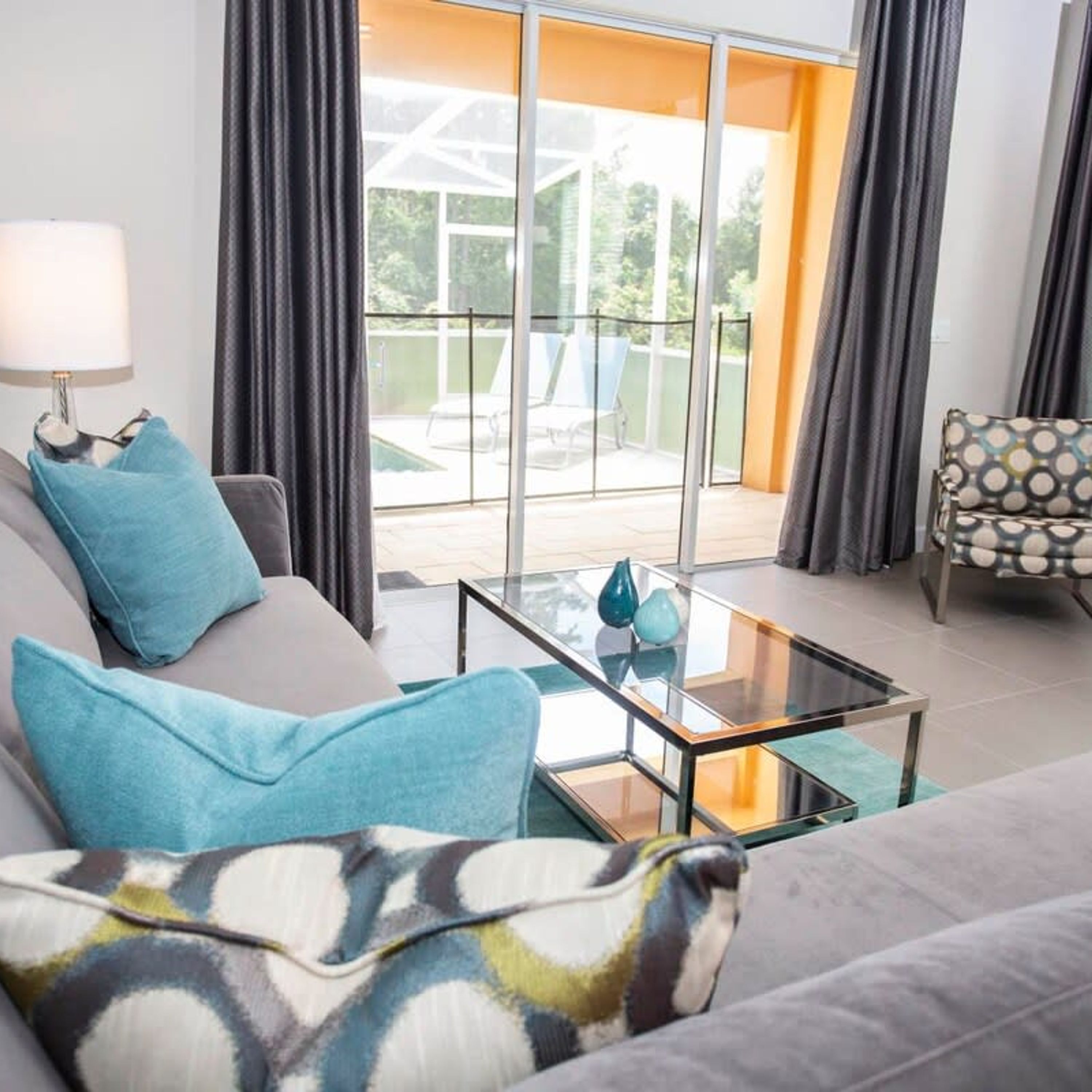 Un salon moderne avec un canapé, un coussin décoratif à motifs, une table basse en verre et un fauteuil avec un coussin à pois.