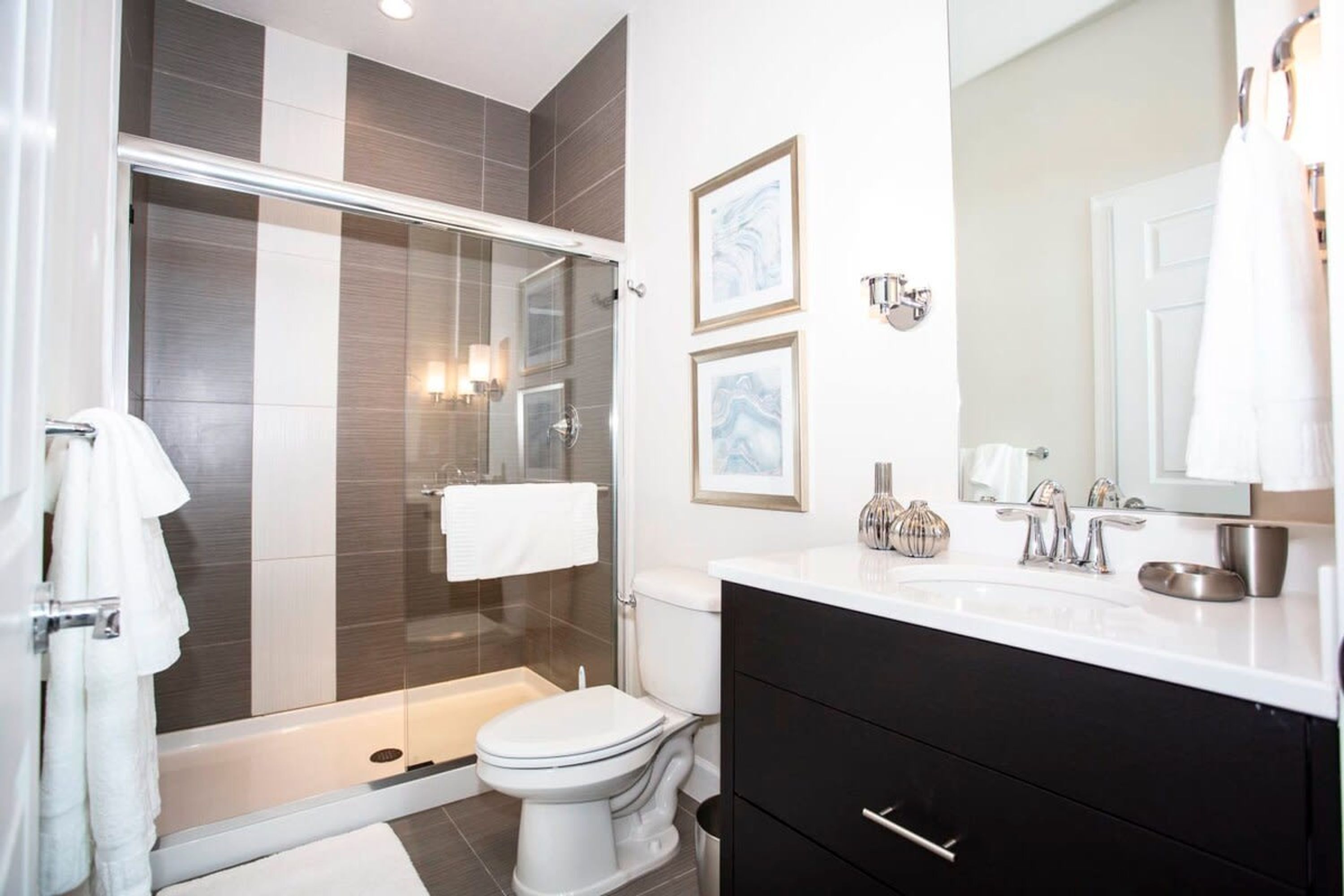 A modern bathroom with a glass-enclosed shower, a white toilet, and a black vanity with a mirror.