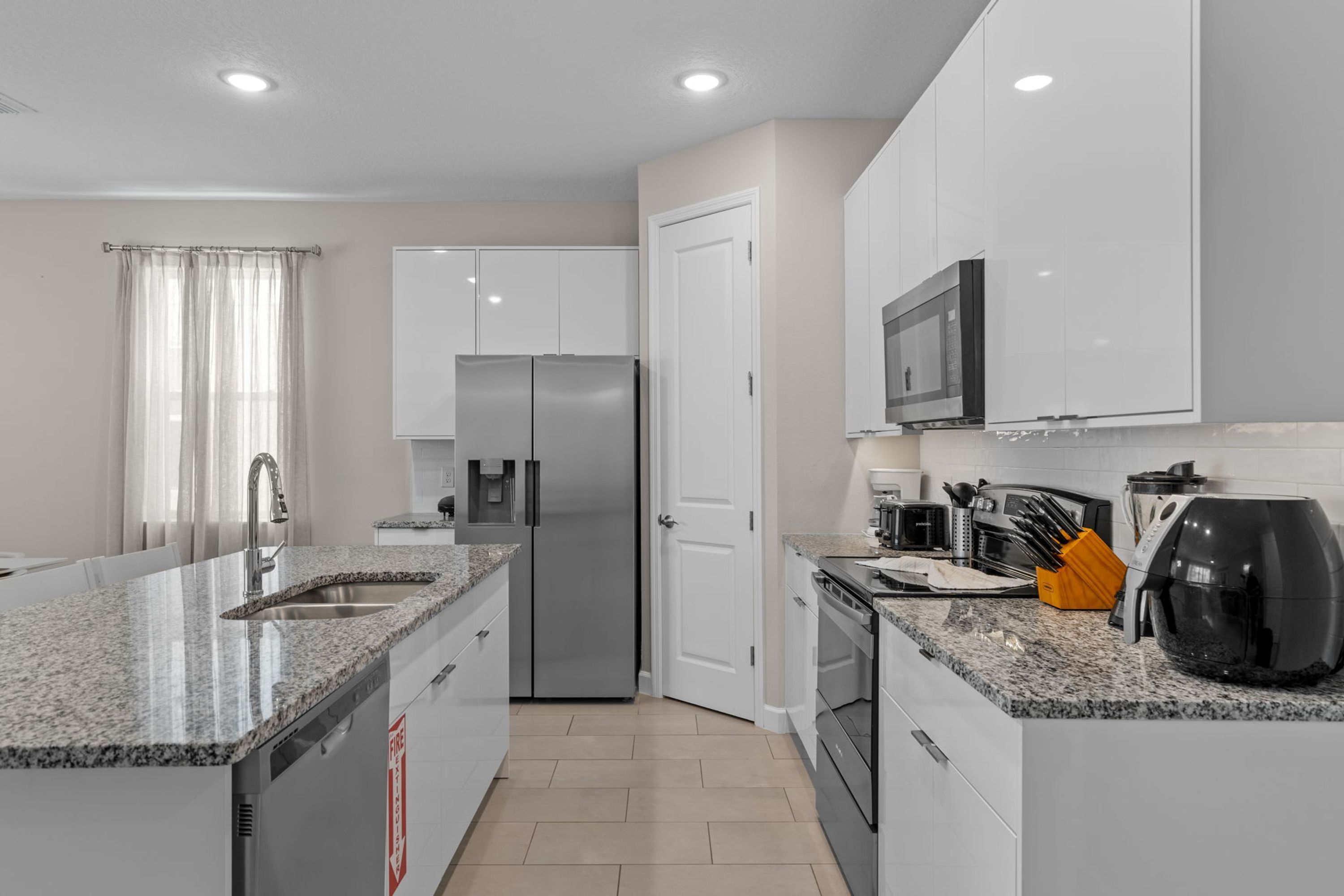 A modern kitchen with white cabinets, stainless steel appliances, granite countertops, and a built-in oven.