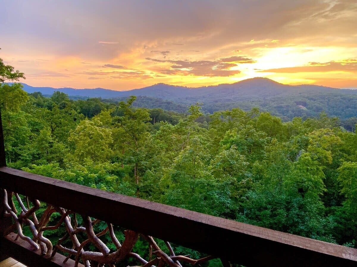 Un balcón con vista a un paisaje boscoso y una cordillera al atardecer.