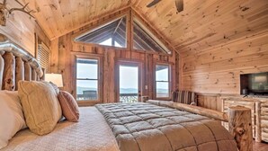 Une chambre dans un chalet en bois, avec un grand lit, une télévision et un balcon offrant une vue panoramique.