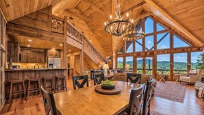 A spacious wooden interior with a dining area, kitchen, and large windows offering a view of the outdoors.