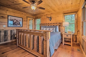 L'intérieur d'une cabane en bois, avec un lit, un bureau, un ventilateur de plafond et un tableau encadré accroché au mur.