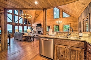 A spacious kitchen with a stainless steel dishwasher, granite countertops, and a large window overlooking a scenic view.