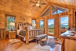 A wooden cabin interior with a bed, a bench, a dining table, and a view of the outdoors.