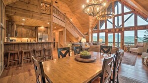 Un intérieur spacieux en bois, avec une grande table à manger, un escalier et une vue dégagée grâce à de grandes fenêtres.