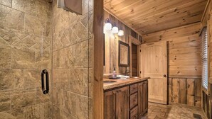 A wooden cabin bathroom with a shower, a sink with a mirror, and a door.
