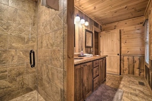 A wooden cabin bathroom with a shower, a sink with a mirror, and a door. - Long-Range Views | Game Room | Fire Pit | Pets (Blue Ridge)