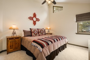 A bedroom with a bed, two nightstands, a wall-mounted lamp, a window with blinds, and a ceiling fan.