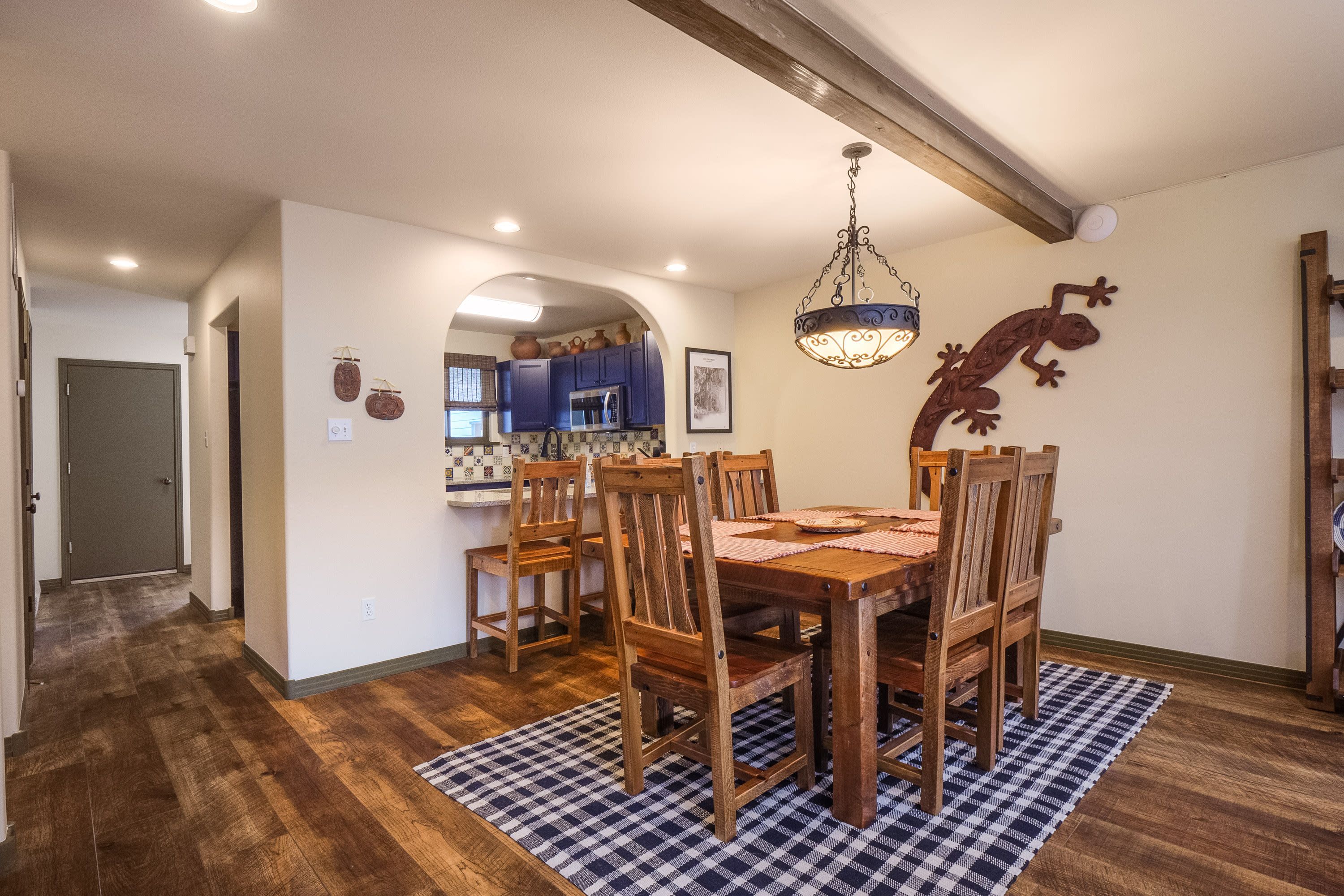 Un comedor con mesa y sillas de madera, un tapete a cuadros y una cocina al fondo.