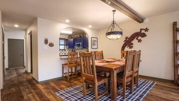 Un comedor con mesa y sillas de madera, un tapete a cuadros y una cocina al fondo.