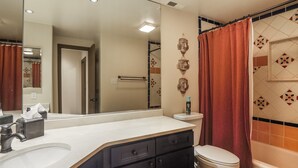 Un baño con lavamanos blanco, inodoro, cortina de ducha y espejo.