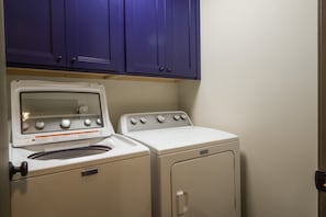 A laundry room with a white Maytag washer and dryer, a blue cabinet above, and a wooden countertop.