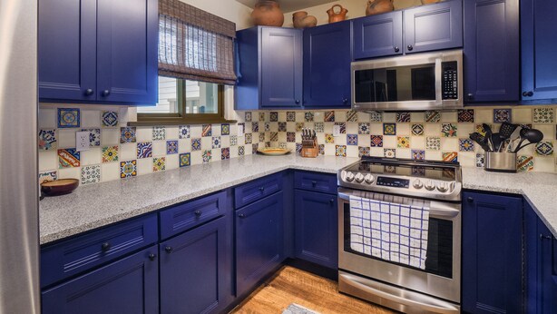 Una cocina con armarios azules, microondas, estufa y salpicadero de azulejos.