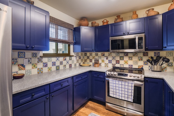A kitchen with blue cabinets, a stainless steel refrigerator, a microwave, and a stove.
