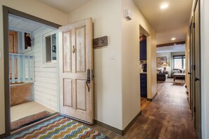 A hallway with a wooden door, a doormat, and a light switch on the wall.