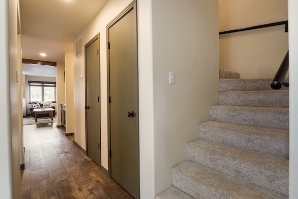 A hallway with a carpeted floor leading to a staircase with a handrail.