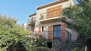 Un edificio di due piani con balconi, una scala e vegetazione circostante.