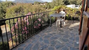 Un balcone con pavimento in pietra, ringhiera in metallo, un tavolo e due sedie.